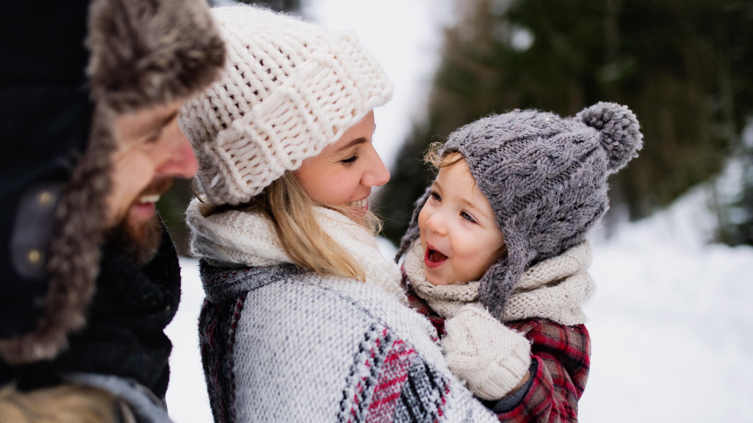 Un couple avec leur enfant rigolent sous la neige - La signature MGM - Profitez de la montagne en hiver