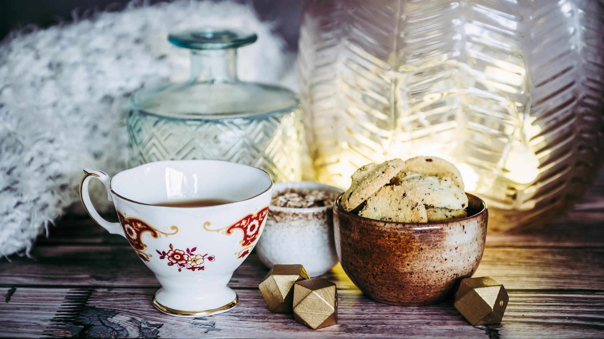 Une tasse de thé et des cookies sont déposées sur une table, à côté de vases et d'un plaid en laine
