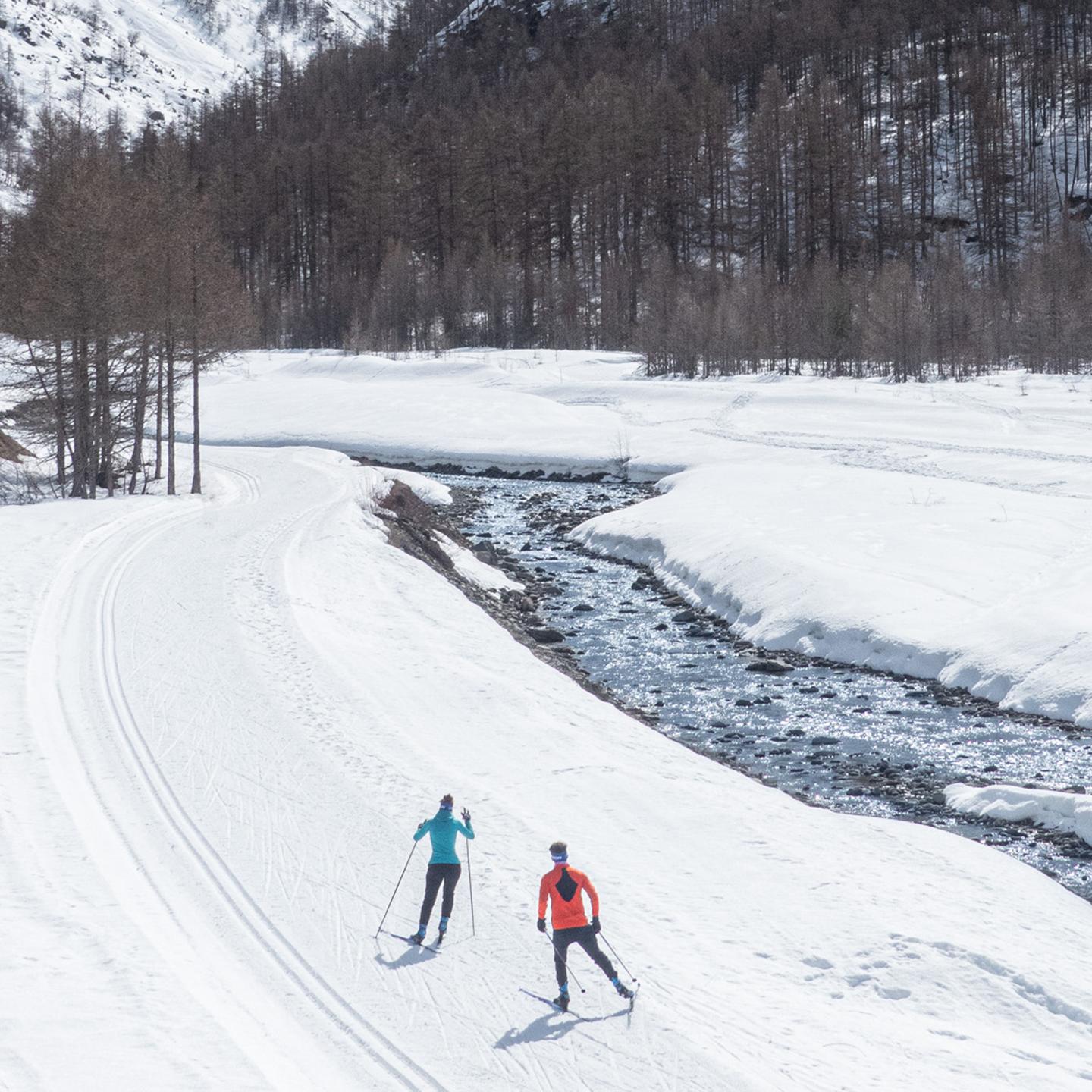 Deux personnes font du ski nordique le long d'un cours d'eau en Haute Maurienne