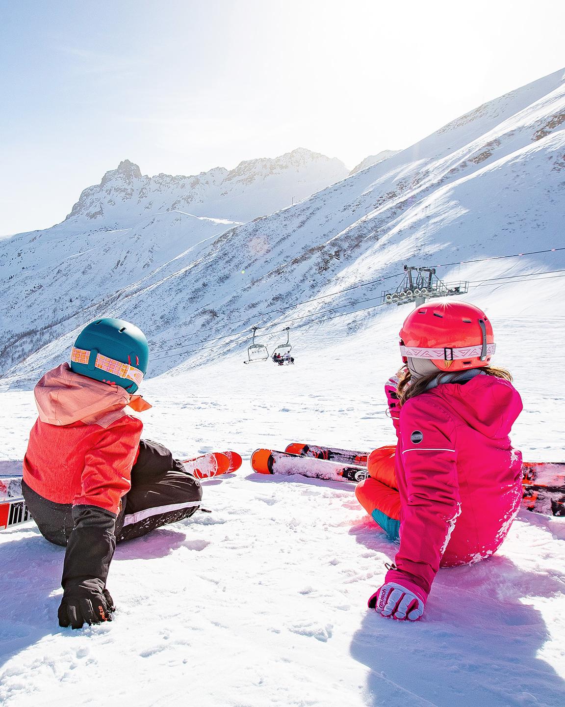 3 enfants à skis sont assis de dos et regardent la vue sur les pistes du Grand Domaine