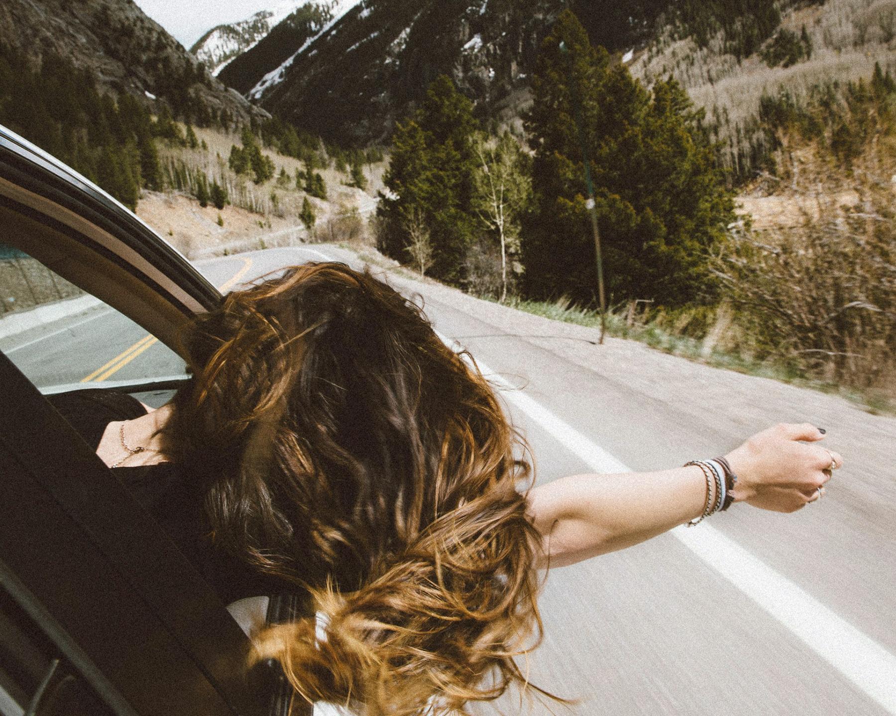 Une femme du côté passage d'une voiture a passé sa tête la fenêtre , elle prend l'air en roulant, la main droite au vent